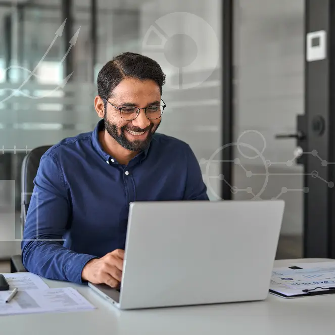 A man wearing glasses is focused on his laptop, engaged in work at a desk.